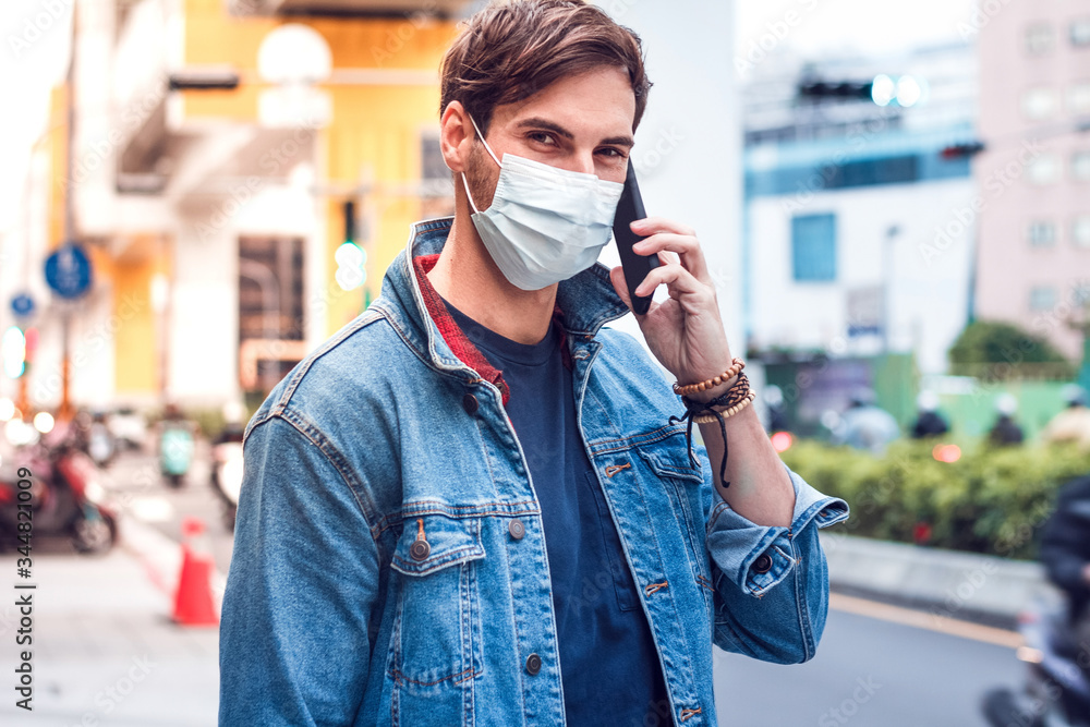 A mature handsome man with a beard talking on his mobile phone and wears a face pollution mask to protect himself from coronavirus on the street.