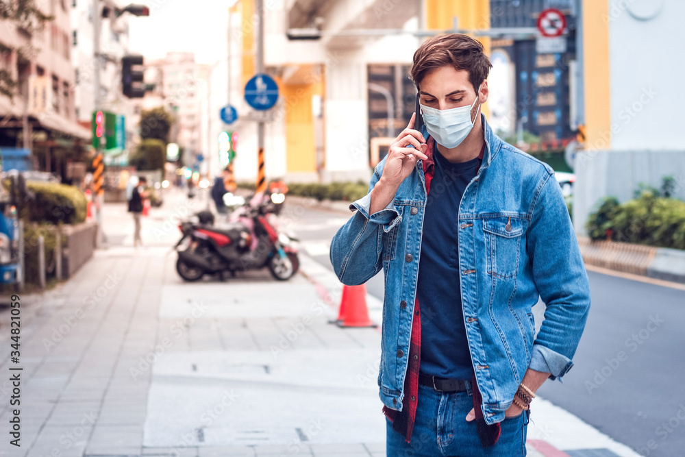 Fototapeta premium A mature handsome man with a beard talking on his mobile phone and wears a face pollution mask to protect himself from coronavirus on the street.