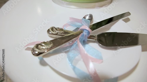 Silver cake spatula, knife and two teaspoons wrapped in blue and pink ribbon on a white plate. Birthday, wedding. photo