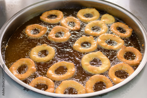 Small donuts being deep fried in boiling oil in a large pan, at a street food market, top view or flat lay photo of healthy food photographed with selective focus 