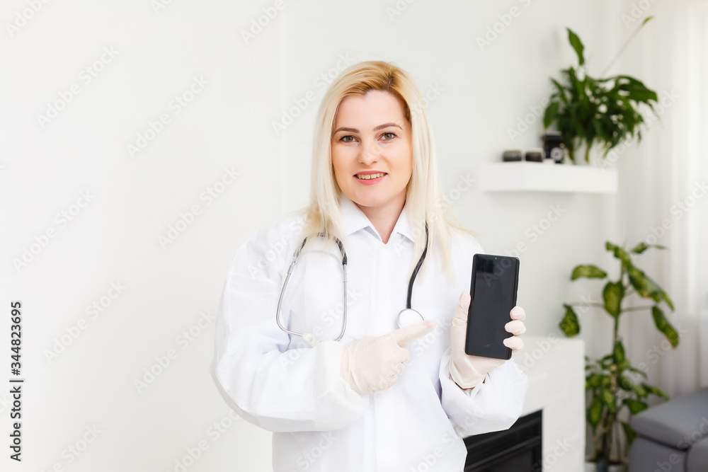 Side profile portrait smiling female doctor, healthcare professional in white lab coat with stethoscope, analyzing data results on mobile smart phone standing in hospital hallway corridor