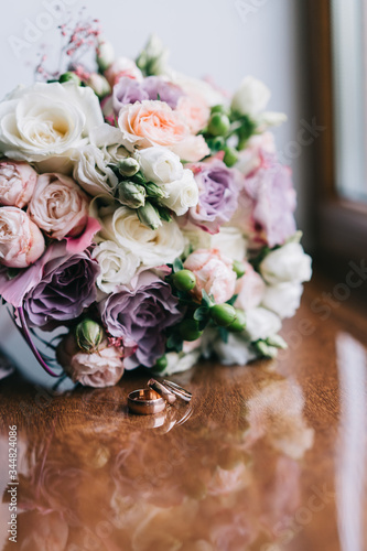 Wedding bouquet with white pink yellow roses and greenery on a wooden background with a pink ribbon with three wedding rings