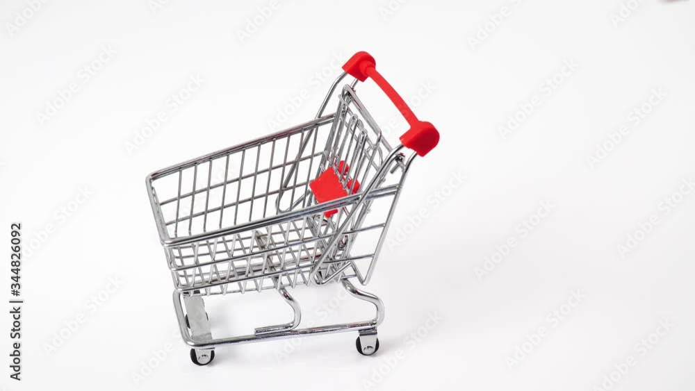 Hand pushing miniature toy supermarket trolley. White background. Place for text. Shopping concept. Hand pushing miniature toy supermarket trolley. White background. Place for text. Shopping concept.