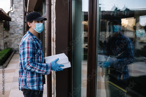 Courier in protective mask delivers parcel, customer in medical gloves receives box. Delivery service under quarantine, disease outbreak, coronavirus covid-19 pandemic conditions.