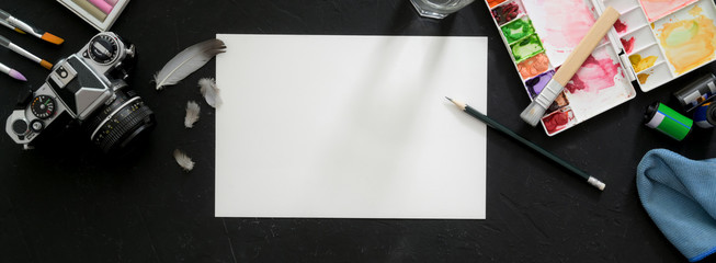 Top view of artist workspace with sketch paper, painting tools, camera and other supplies