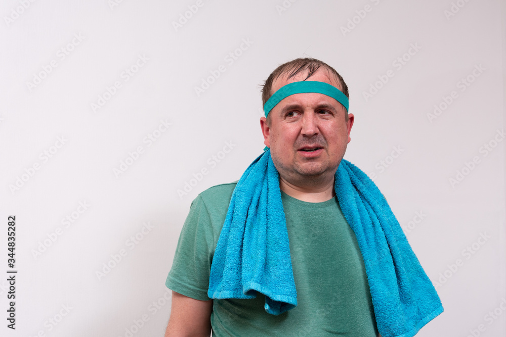 Funny fat man in a green bandana and t-shirt with a blue towel around his neck. half-length portrait. home fitness training, independent training. Funny fat man in a green bandana and t-shirt with a blue towel around his neck. half-length portrait. home fitness training, independent training.