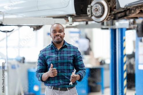 Auto mechanic repairing a car, standing over a raised car on a lift, showing cool, holding a wrench in his hand