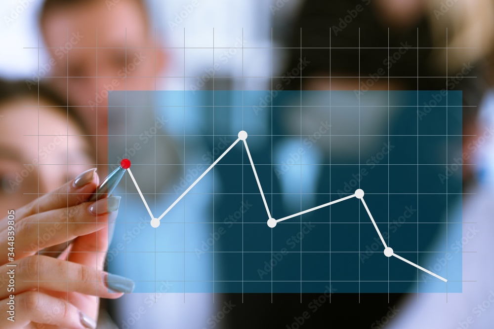 A group of people examines the financial statistics of an enterprise pointing with a hand with a pen on the graph point A group of people examines the financial statistics of an enterprise pointing with a hand with a pen on the graph point