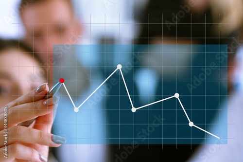 A group of people examines the financial statistics of an enterprise pointing with a hand with a pen on the graph point