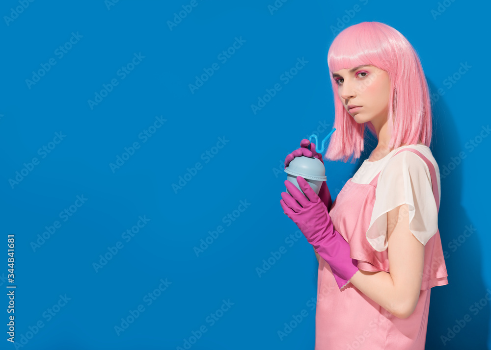 Girl pink hair drinking from disposable blue plastic cup. Teenager holding summer cocktail in protective gloves on blue background. Advertising of protection during coronavirus. Copy space Girl pink hair drinking from disposable blue plastic cup. Teenager holding summer cocktail in protective gloves on blue background. Advertising of protection during coronavirus. Copy space