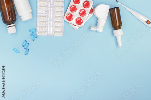 Various medicines, a thermometer, sprays from a stuffy nose and a pain in a throat on a blue background.