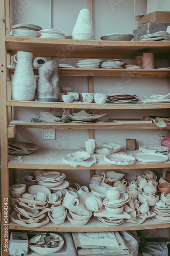 A shelf with lots of craft tableware. A pottery studio with drying clay pots  dishes  mugs  bowls  jugs  vases and cups. A workshop concept. A uniques design of plates. Handmade china