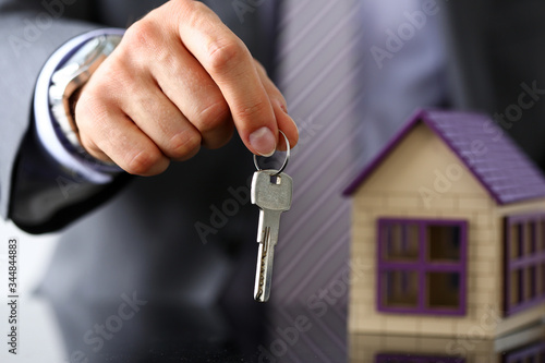 Man in suit and tie hold in hand silver key giving it to buyer closeup. New owner, pledge, idea for life, family solution, male arm, credit negotiation, clerk in office, future plan concept