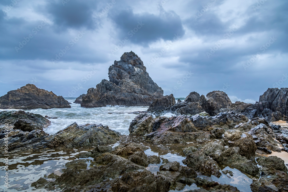 Long Exposure of rocks at the beach of the Camel Rock bay in New South Wales, Australia at a cloudy and windy day in summer with strong waves in the ocean. 