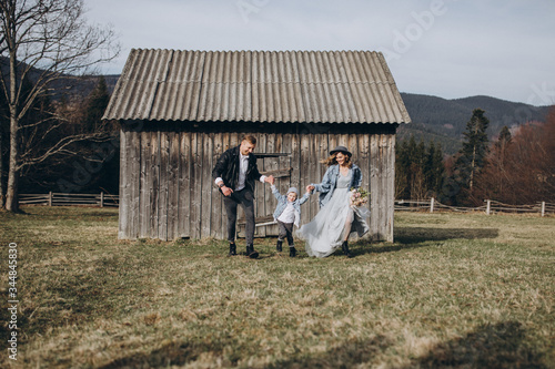 Stylish family in the autumn mountains. Stock photo. A guy in a leather jacket and a young girl in a gray-blue dress with his son on the background of an old wooden barn at sunset © AlexGukalovUkraine