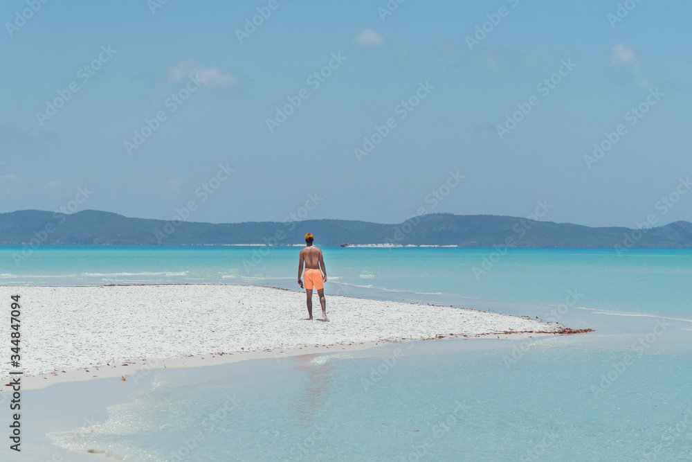 Man on paradise blue beach. Tourist on Whitsundays beach, white sand, in orange shorts, hat with aqua turquoise ocean. Travel, beauty, holiday, vacation, exotic. Whitsundays Islands, Australia.