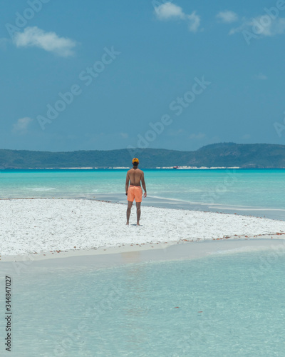 Man on paradise blue beach. Tourist on Whitsundays beach  white sand  in orange shorts  hat with aqua turquoise ocean. Travel  beauty  holiday  vacation  exotic. Whitsundays Islands  Australia.