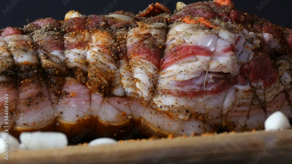 Fresh juicy piece of raw meat pork steak or bacon with seasonings of pepper, garlic, carrots in rustic style rewound with baking threads in the oven salted and spiced, garnished on wooden background. Fresh juicy piece of raw meat pork steak or bacon with seasonings of pepper, garlic, carrots in rustic style rewound with baking threads in the oven salted and spiced, garnished on wooden background.