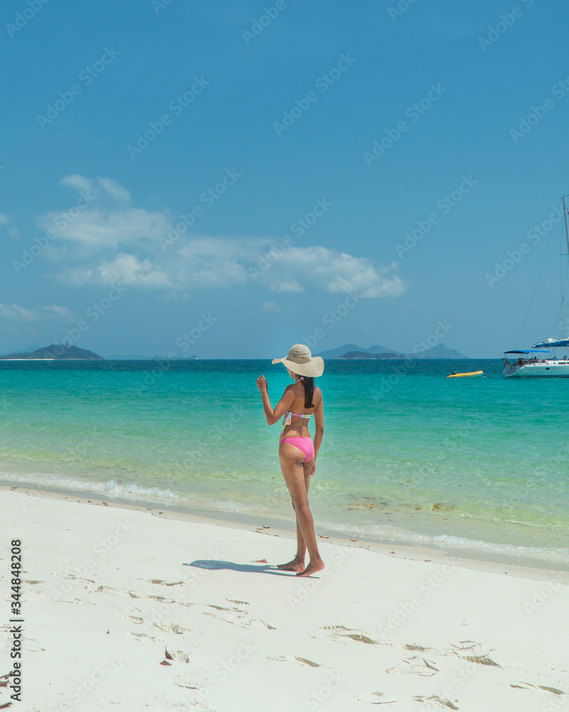 Woman on paradise blue beach. Tourist on Whitsundays beach, white sand, in pink bikini & hat, with aqua turquoise ocean. Travel, holiday, vacation, paradise, exotic. Whitsundays Islands, Australia.