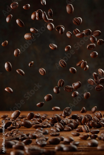 Many roasted coffee beans flying/ falling in the air over a wooden table. Selective focus