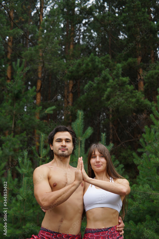 Fototapeta premium Healthy lifestyle, sport, yoga and people concept - beautiful couple doing yoga together over green woods background