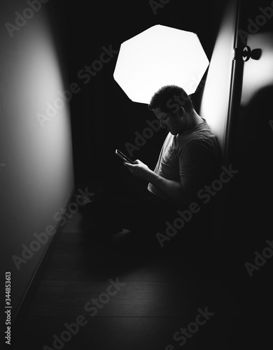 Man silhouette sitting on a corridor bored with the phone in hand dark shot back lit