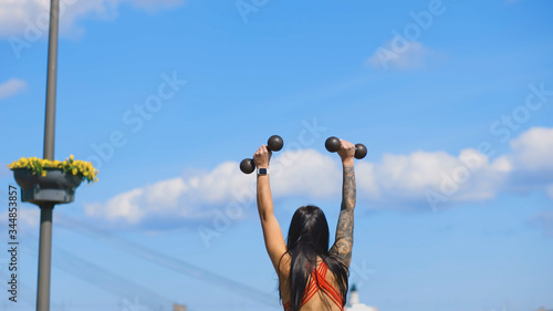 Backside view of happy woman lifting dumbbells outdoors