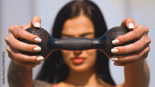 Fit brunette woman holds old dumbbell during sunny day and looks at you