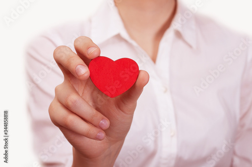 Young girl in a white blouse holds a small red wooden heart. The concept of love  relationships  friendship  protection