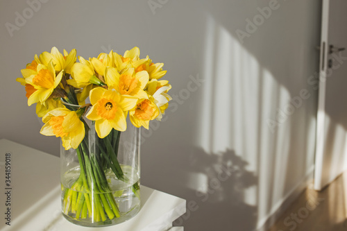 Carta da parati Yellow daffodils in a glass vase standing in a sunny room.