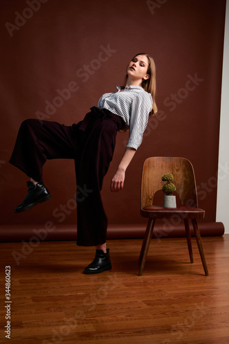 Gorgeous young female in classic suit, black shoes and grey coat. Vintage chair. Woman's clothes.