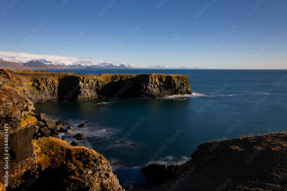 Basalt Rock cliffs fall away into the calm sea below. Taken from Iceland’s, Snafellsnes peninsula on a clear blue sky day. 
