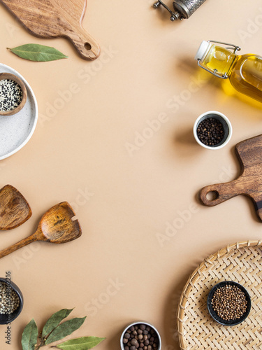 Frame of small bowls various dry spices, wood kitchen utensils, olive oil in glass bottle on beige background. Top view. copy space