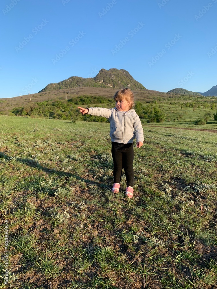 A girl of three years old plays in nature. Cheerful little beautiful girl on the grass. Happy little kid in the fresh air.