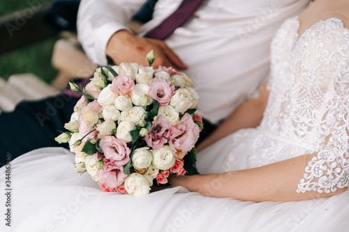 Wedding bouquet in the hands of the bride with white pink yellow roses and greenery on a beige background