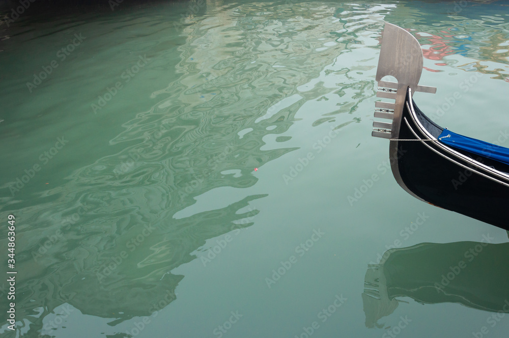 Fragment of a gondola sailing through a channel in Venice. Abstract reflections in the water