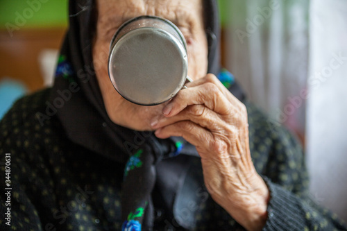 Old woman drinking out of the metal mug.