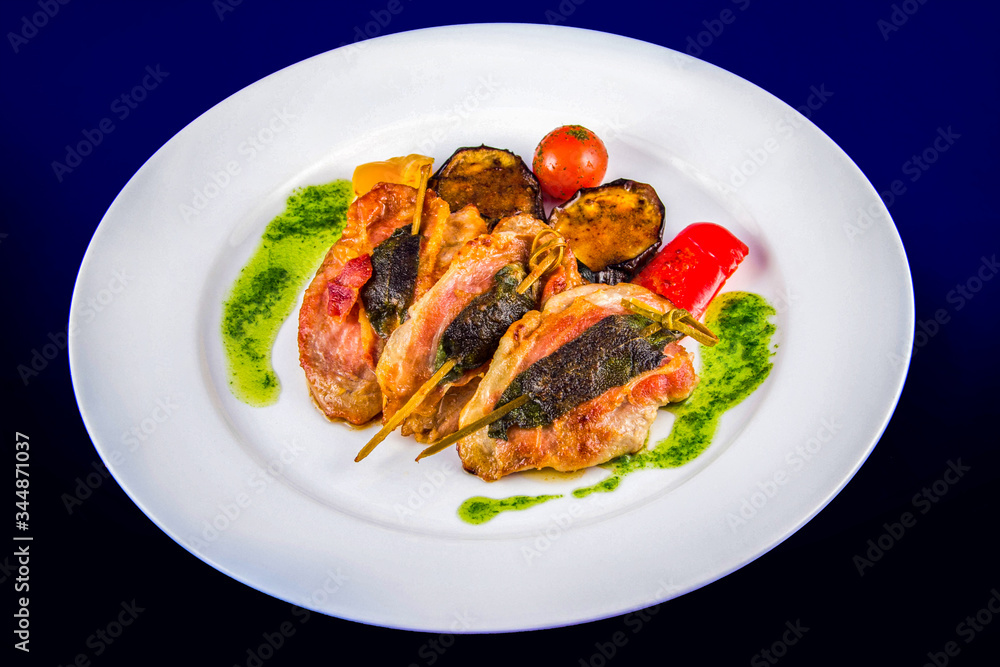 Turkey medallions stuffed with herbs on skewers with grilled vegetables and pesto sauce. Flat lay top view on a white plate on a blue background. Turkey medallions stuffed with herbs on skewers with grilled vegetables and pesto sauce. Flat lay top view on a white plate on a blue background.