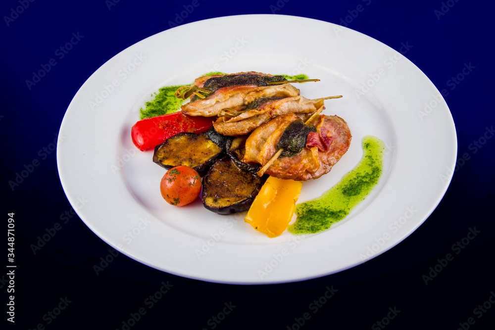 Turkey medallions stuffed with herbs on skewers with grilled vegetables and pesto sauce. Flat lay top view on a white plate on a blue background. Turkey medallions stuffed with herbs on skewers with grilled vegetables and pesto sauce. Flat lay top view on a white plate on a blue background.