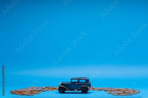 Blue car figurine surrounded by a bunch of coins, on blue background.