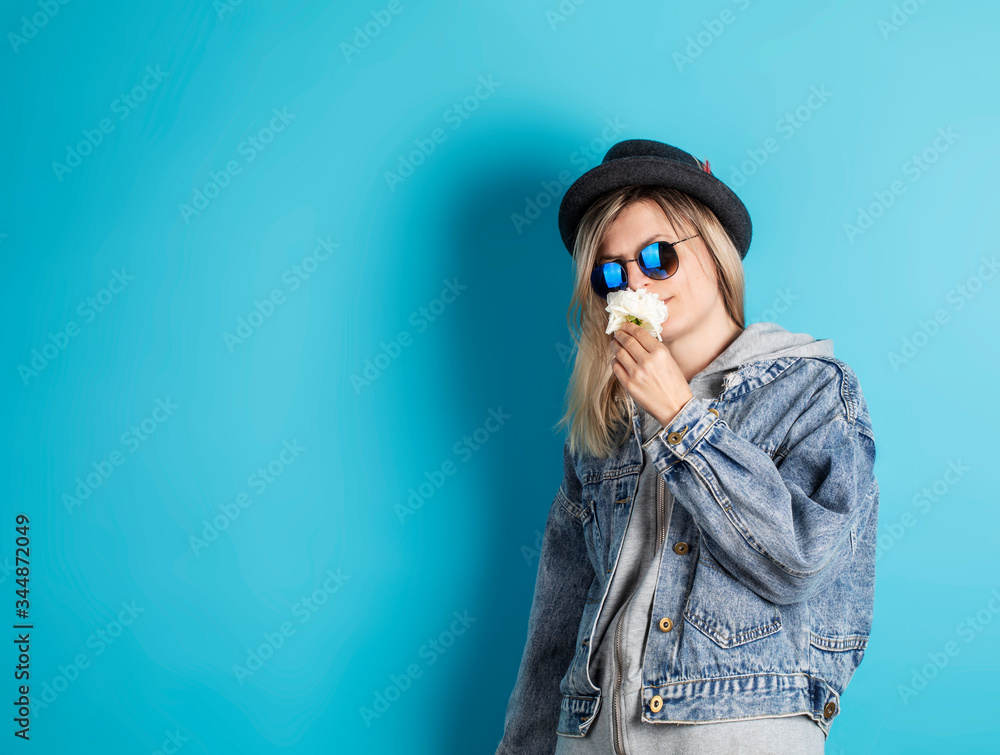 Trendy hipster girl. Caucasian young woman with sunglasses, hat and flower in hand standing near promotional copy space background Trendy hipster girl. Caucasian young woman with sunglasses, hat and flower in hand standing near promotional copy space background