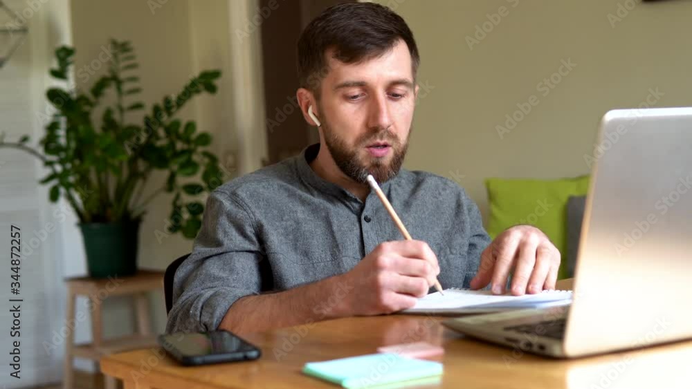 Handsome Eastern European man studying remotely at home during Corona virus quarantine lockdown, writing down during online courses Handsome Eastern European man studying remotely at home during Corona virus quarantine lockdown, writing down during online courses