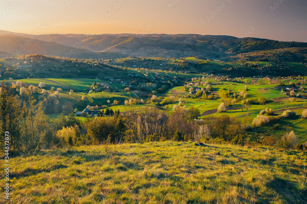 Majestic light in the spring mountains rural landscape. Sun light up blossom cherry trees and green meadows and agricultural fields. Village Hrinova in Slovakia