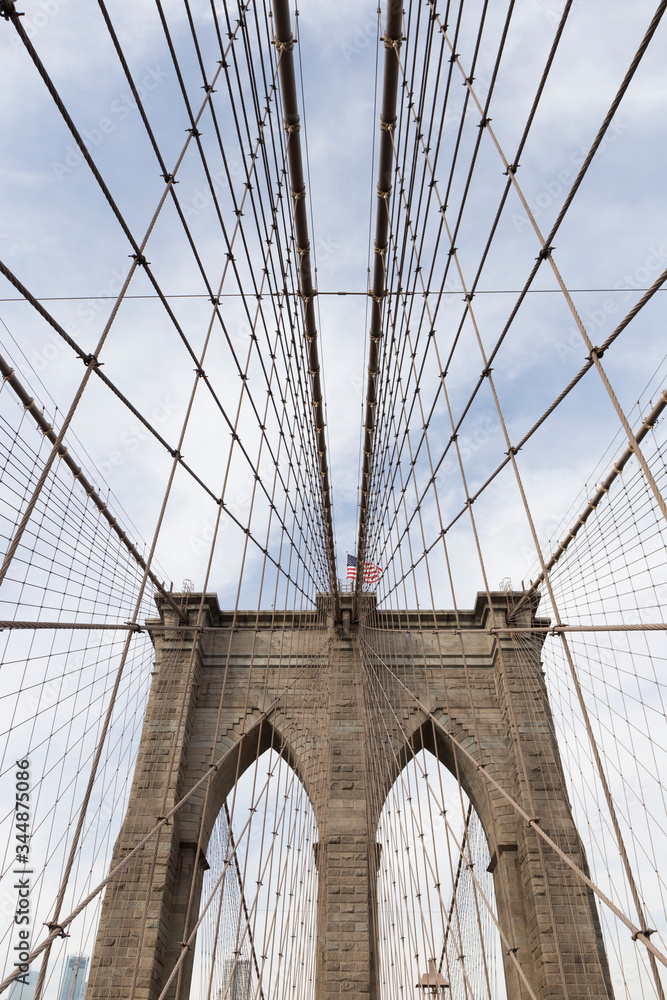 Fototapeta premium Brooklyn Bridge, photo from inside the bridge, perspective of one of the arches with the cables creating geometric shapes in the sky, in the middle you can see the US flag, photographs of New York