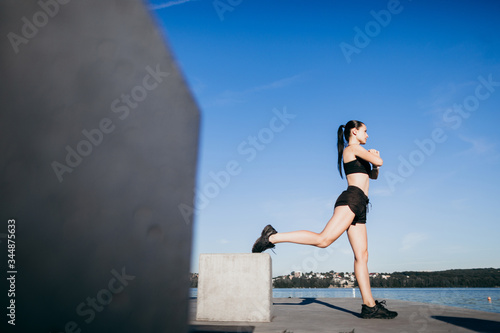 Athletic girl dressed in black doing exercises, squats on city beach in the morning