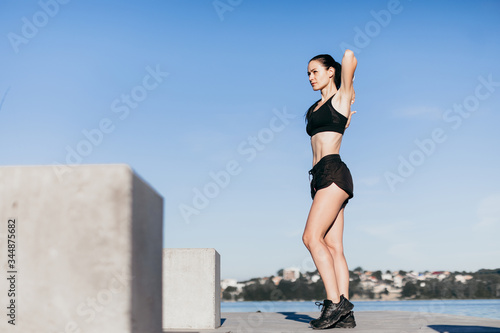 sports girl, dressed in black, warms up before running, at the playground on city beach in the morning