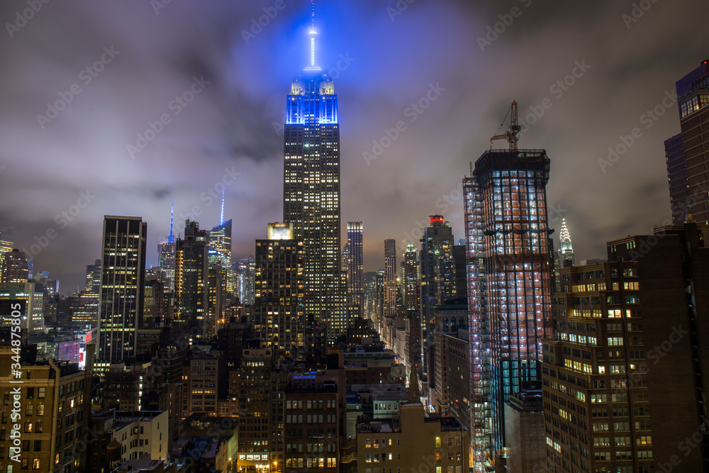 Fototapeta premium empire state building illuminated with a blue light at night, illuminated Manhattan buildings viewed from a rooftop