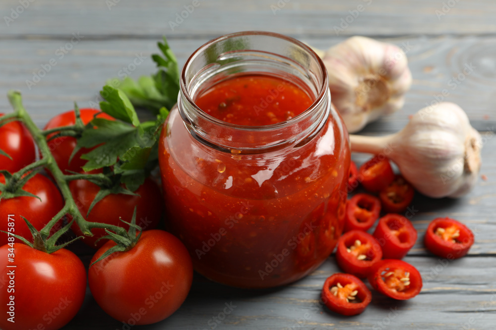 Jar with red chilli and tomato sauce, and spices on wooden table Jar with red chilli and tomato sauce, and spices on wooden table