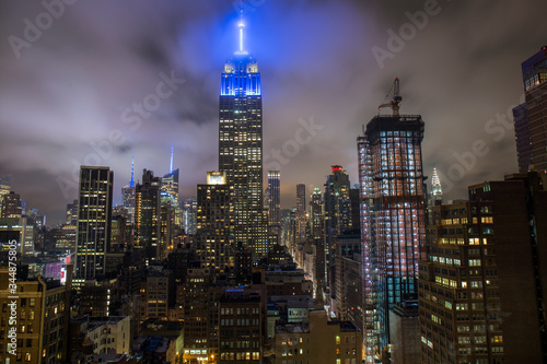 empire state building illuminated with a blue light at night, illuminated Manhattan buildings viewed from a rooftop