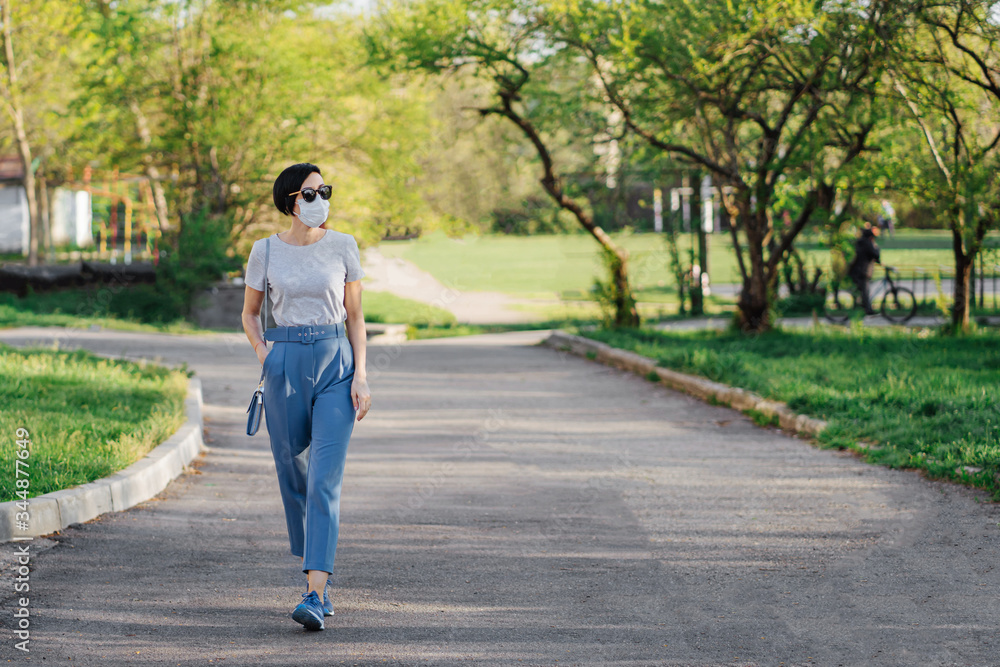Woman wearing medical mask, alone walks in the park during Covid 19 outbreak. Protection in prevention for coronavirus. Social Distancing concept. Woman wearing medical mask, alone walks in the park during Covid 19 outbreak. Protection in prevention for coronavirus. Social Distancing concept.